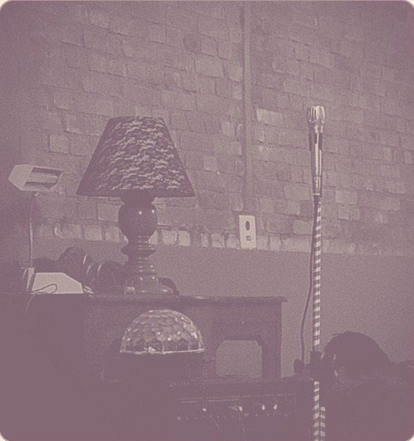 A warm lamp-lit room with a brick wall and a microphone on a stand